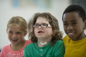 A multi-ethnic group of elementary age children are sitting together happily in the classroom.